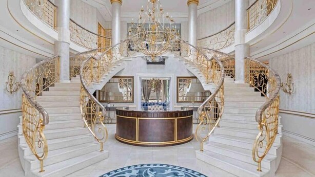 Un intérieur somptueux, à plusieurs niveaux, avec des sols en marbre, des balustrades dorées richement décorées et un lustre central.
