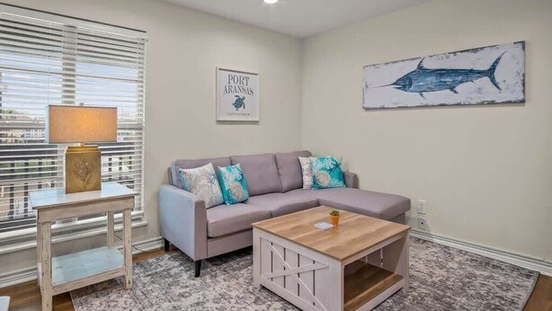 Ein Wohnzimmer mit grauem Sofa, einem Holztisch, einer Lampe und einem Bilderrahmen mit einem Fisch an der Wand.