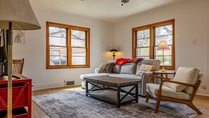 A living room with a sofa, armchair, coffee table, and a red bookshelf.