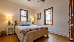 A bedroom with a bed, two bedside tables, a nightstand, a lamp, a framed picture, and a window.
