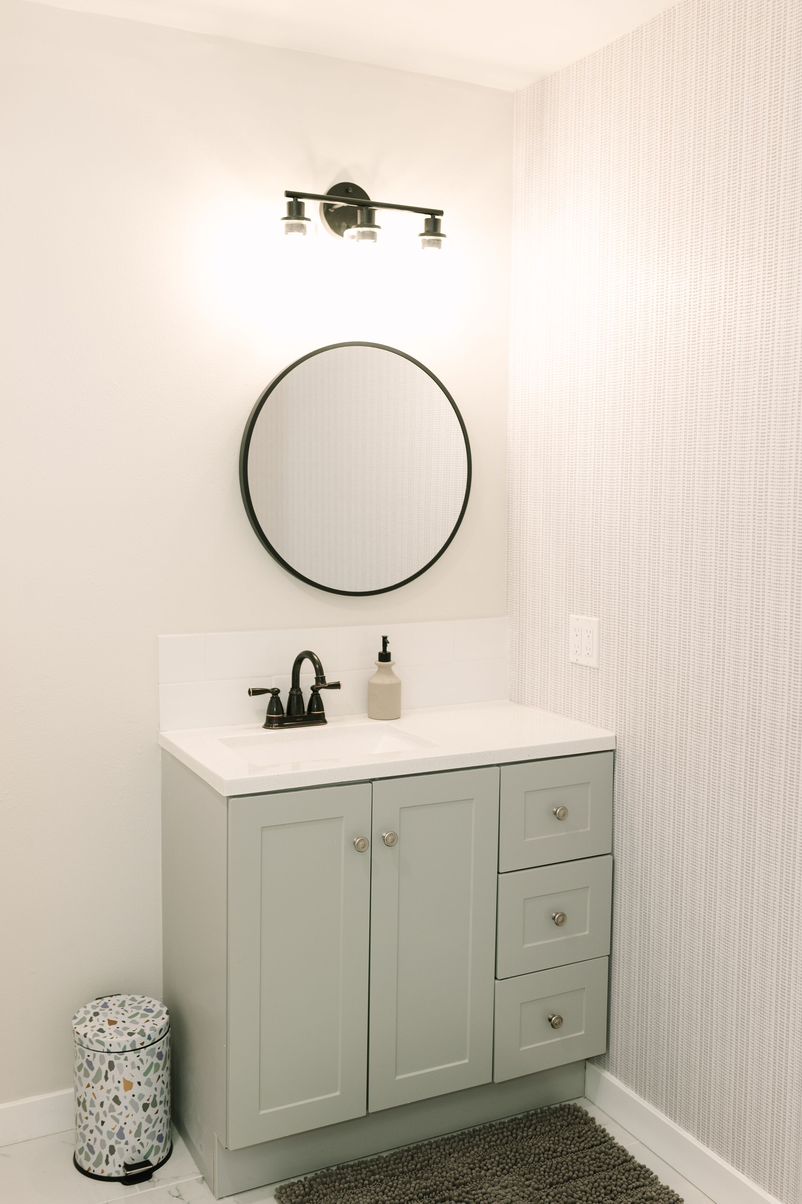 A bathroom with a white sink, a round mirror, and a light fixture above the mirror.