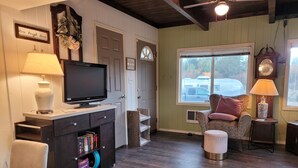 A cozy living room with a television, books, a coffee table, and a comfortable chair. - Cozy cottage with river access and great outdoor adventures (La Pine)