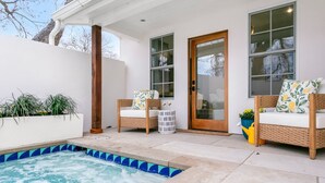 Un espacio al aire libre techado con un jacuzzi, dos sillones de mimbre con cojines y una planta en maceta.