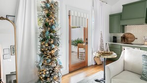 Una sala de estar moderna con un árbol de Navidad alto y decorado, una zona de cocina verde y un sofá blanco.