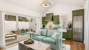 A modern kitchen with green cabinets, a stainless steel refrigerator, and a dining area with a light blue sofa and a coffee table. - Bijou: Collette | Luxury Cottage | Plunge Pool | Full Kitchen | Seasonal Fireplace (Fredericksburg)