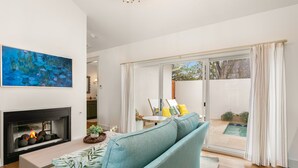 A modern living room with a fireplace, a sofa, and a view of a pool through large sliding doors. - Bijou: Collette | Luxury Cottage | Plunge Pool | Full Kitchen | Seasonal Fireplace (Fredericksburg)