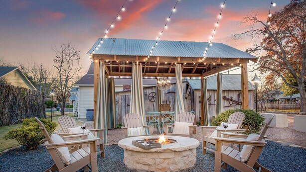 An outdoor seating area with Adirondack chairs and a stone fire pit. - Bijou: Chloe | Luxury Cottage | Plunge Pool | Full Kitchen | Seasonal Fireplace (Fredericksburg)