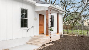 A white house with a front porch, a wooden door, and a mailbox. - Bijou: Chloe | Luxury Cottage | Plunge Pool | Full Kitchen | Seasonal Fireplace (Fredericksburg)