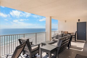 A balcony with a view of the ocean, a dining table, chairs, and a sofa.