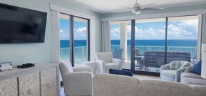 A balcony with a view of the ocean, a television, and a seating area with chairs and a table.