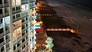 Un hotel moderno de gran altura con varios balcones, un área de piscina con tumbonas y vista al mar.