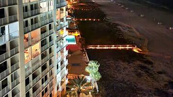A high-rise hotel with multiple balconies, a pool area with sun loungers, and a beach view.