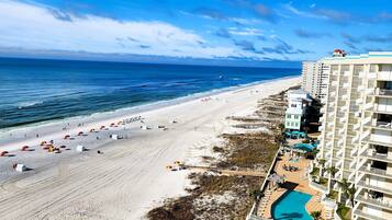 A beachside hotel with a pool, beach umbrellas, and a boardwalk.