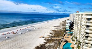 A beach resort with a swimming pool, beach umbrellas, and a hotel building.