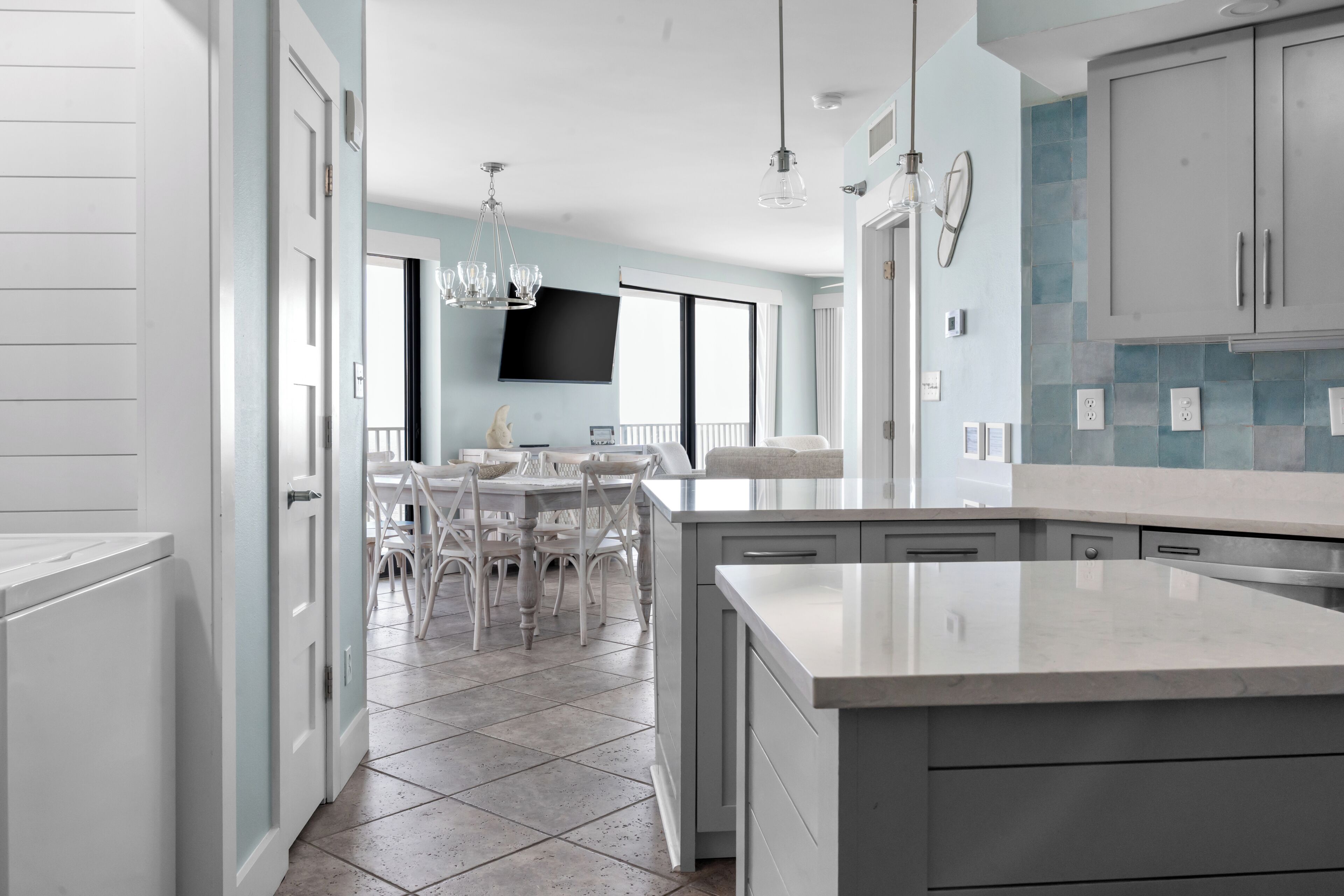 A modern kitchen with a large island, white cabinetry, and a dining area with a white table and chairs.