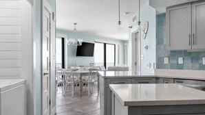 Una cocina moderna con una isla grande, armarios blancos y un comedor con una mesa y sillas blancas.
