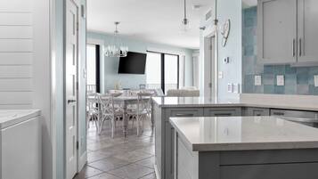 A modern kitchen with a large island, white cabinetry, and a dining area with a white table and chairs.