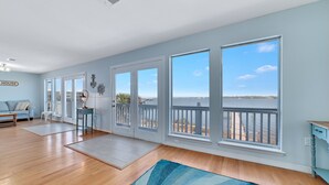A spacious living room with hardwood floors, a blue rug, a sofa, and a view of the ocean through large windows. - WATERFRONT, PRIVATE POOL, GREAT FOR FAMILES & DOG FRIENDLY! (Gulf Shores)