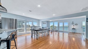 A spacious kitchen with a large island, a dining area with white chairs, and a view of the outdoors through large windows. - WATERFRONT, PRIVATE POOL, GREAT FOR FAMILES & DOG FRIENDLY! (Gulf Shores)