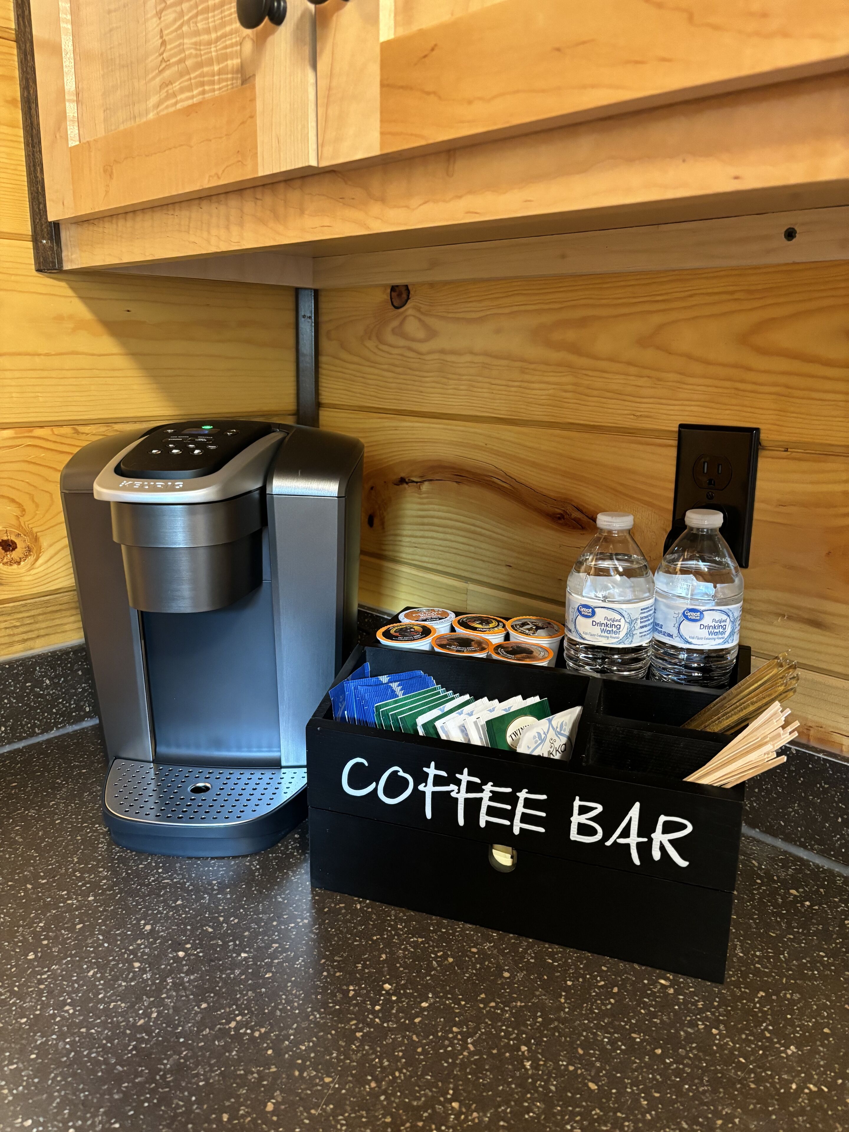 A coffee maker, a box labeled "Coffee Bar," and bottles of water on a countertop.