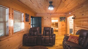 Interior de una cabaña de madera con dos sillones de cuero, techo de madera y una mesita.