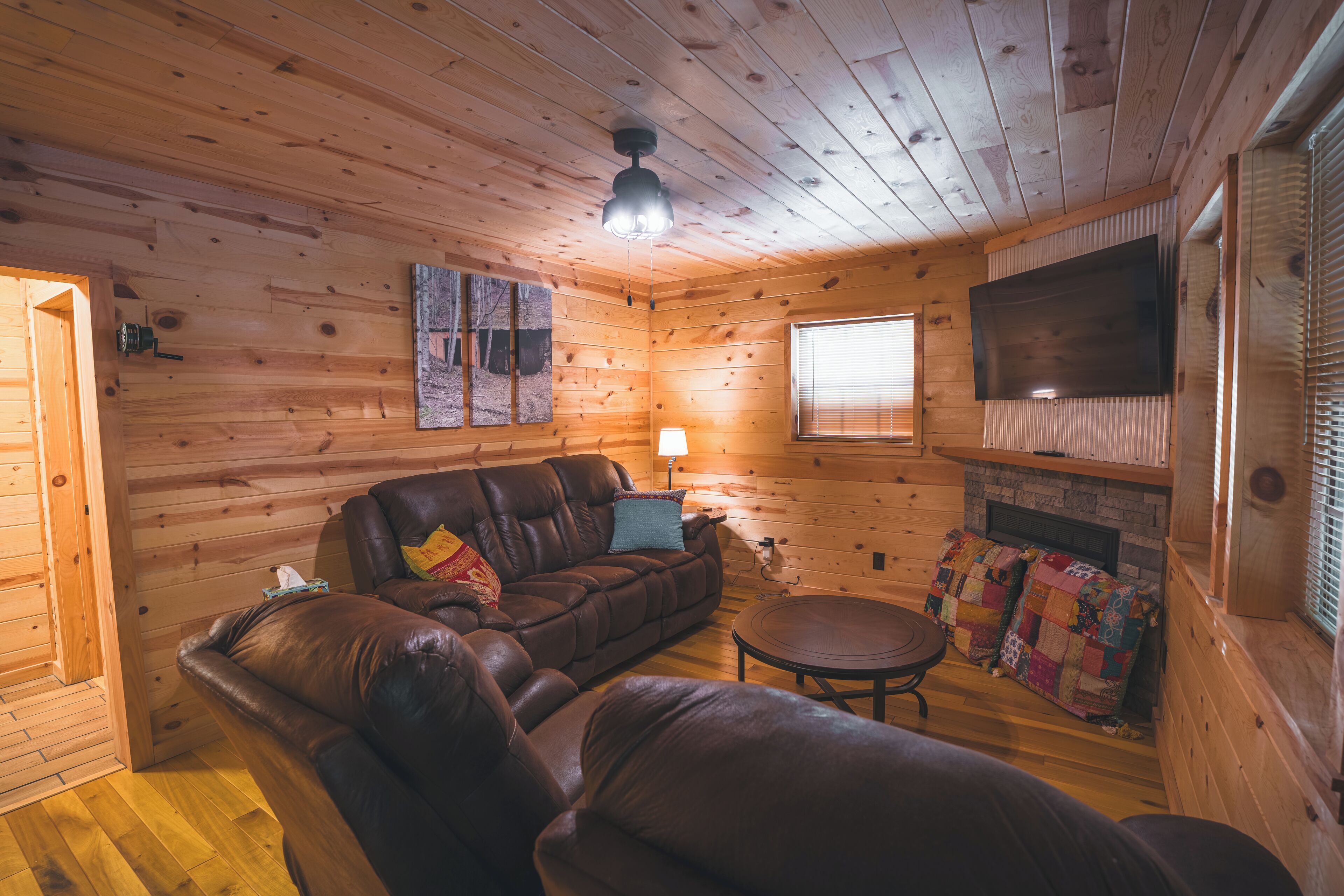 A cozy cabin interior with a leather sofa, a small round table, a quilted blanket, and a mounted TV.