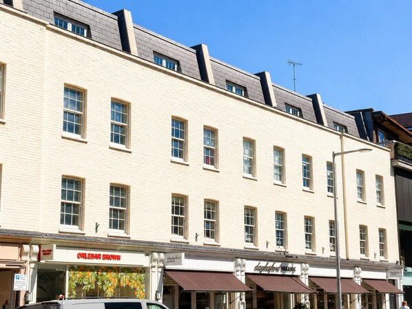 A multi-story building with a flat facade, evenly spaced windows, and a visible ground-floor shop with a sign.