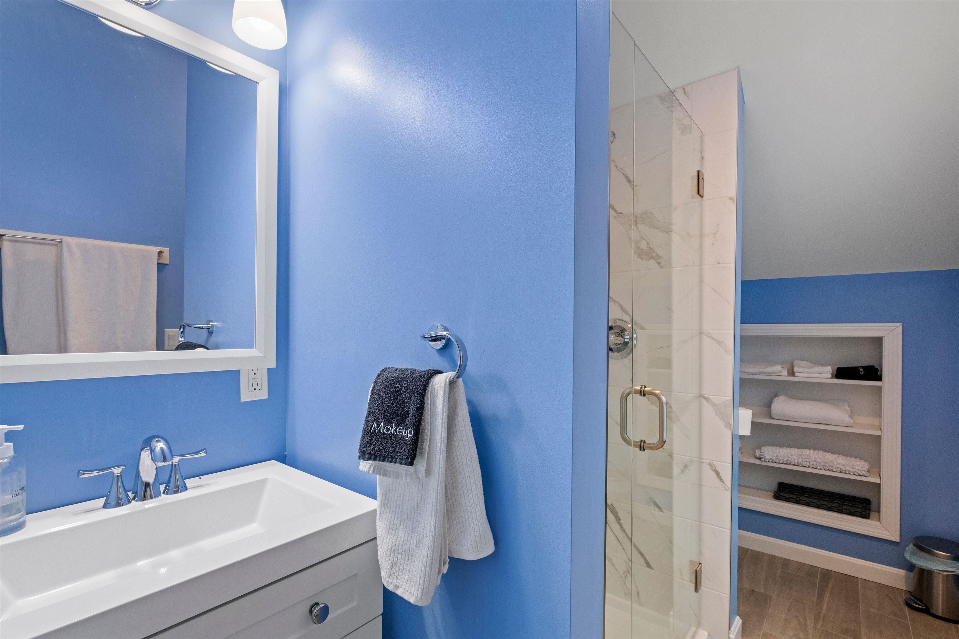 A bathroom with a blue wall, a white sink, a mirror, and a glass shower enclosure.