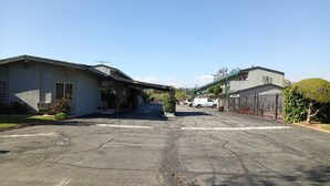 A parking lot with a white van parked in the distance, surrounded by buildings with a flat roof and a covered walkway. - Pomona Inn (Pomona)