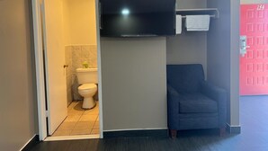 A room with a toilet, a television mounted on the wall, and a blue chair. - Pomona Inn (Pomona)