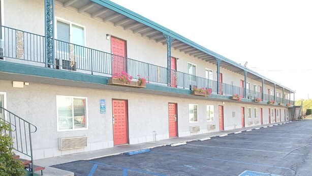 A motel with a row of rooms, each with a red door and a balcony with flowers. - Pomona Inn (Pomona)