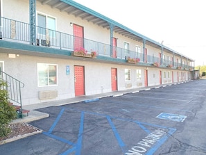 A motel with a row of rooms, each with a red door and a balcony with flowers.