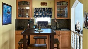 A kitchen with wooden cabinets, a dining table with stools, and a window with a view of the outside.