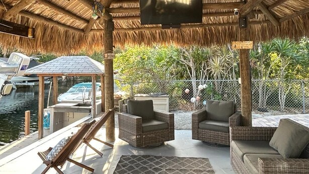 A covered outdoor area with wicker furniture, a fan, and a TV screen.