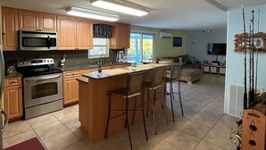 A spacious kitchen with wooden cabinets, a central island with bar stools, a microwave, stove, and a large window.