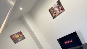 Una sala de estar moderna con un sofá verde, una mesa de centro, un televisor mostrando 'NETFLIX' y dos cuadros en la pared.