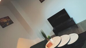 Un salón con un sofá verde oscuro, un televisor de pantalla plana sobre un mueble bajo y dos relojes de pared.