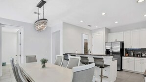Een moderne keuken met witte kasten, een roestvrijstalen koelkast, en een eethoek met een witte tafel en stoelen.