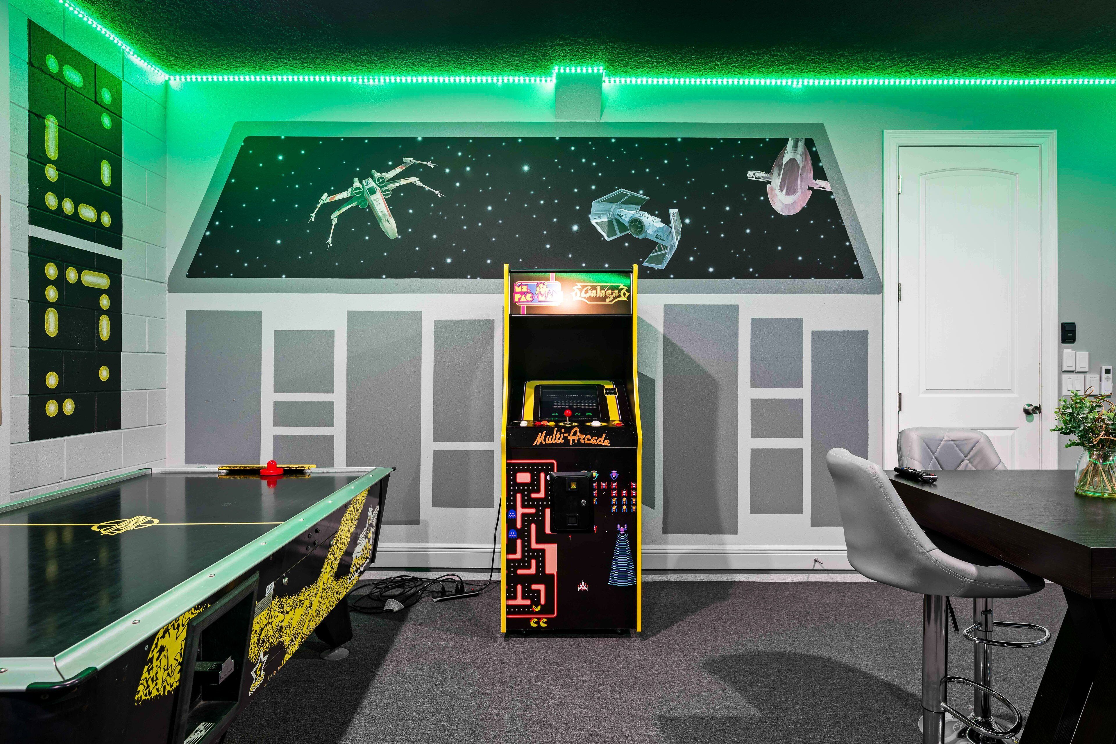 A room with a foosball table, a multi-arcade game machine, and a space-themed wall mural.