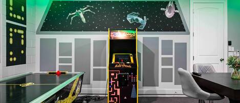 A room with a foosball table, a multi-arcade game machine, and a space-themed wall mural.
