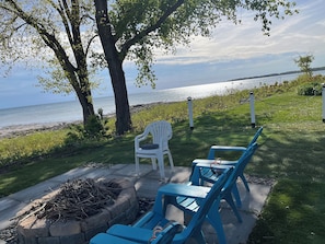 Relax in this serene outdoor seating area overlooking the water, featuring two comfortable chairs and a cozy fire pit.