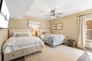 A bedroom with two beds, a ceiling fan, artwork, and a window with curtains.
