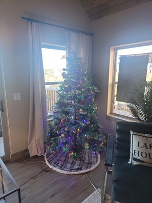 A Christmas tree with lights, placed in a corner with a window and a plant. - New Log Cabin with Private Hot Tub, Free Daily Activities, Arcade & Shuffleboard (Branson)