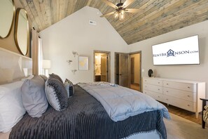 A bedroom with a bed, a dresser, a ceiling fan, and a wall-mounted TV displaying a website.