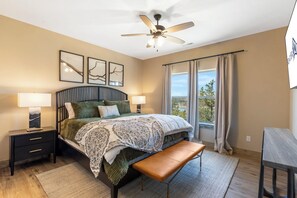 A bedroom with a bed, two bedside tables, a bench, a ceiling fan, and a window with curtains. - New Log Cabin with Private Hot Tub, Free Daily Activities, Arcade & Shuffleboard (Branson)
