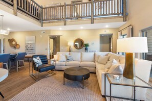 A spacious living area with a high ceiling, a staircase, and a view of the outdoors.