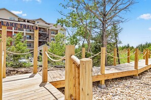 A wooden boardwalk leading to a building labeled 'LAKE TRAIL' with a clear sky and trees in the background.