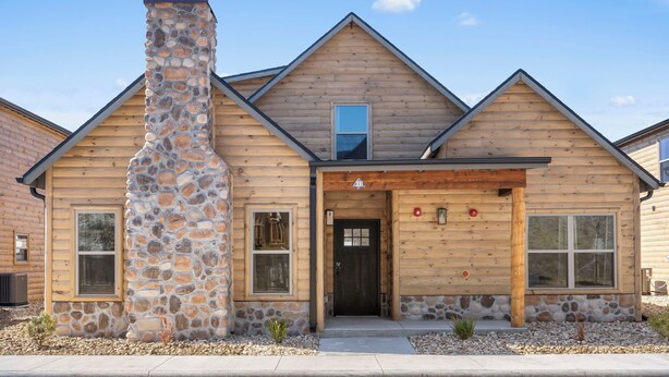 A log cabin with a stone chimney, a front door, and two windows. - New Log Cabin with Private Hot Tub, Free Daily Activities, Arcade & Shuffleboard (Branson)