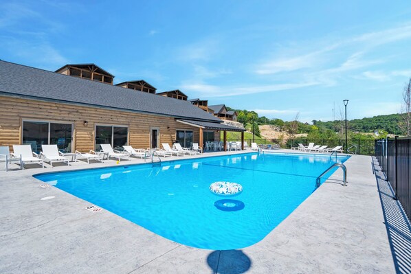 A swimming pool with lounge chairs and a wooden building in the background.