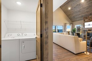 Ein Waschraum mit Waschmaschine und Trockner, ein Wohnzimmer mit Sofa und Fernseher sowie eine Steinsäule.